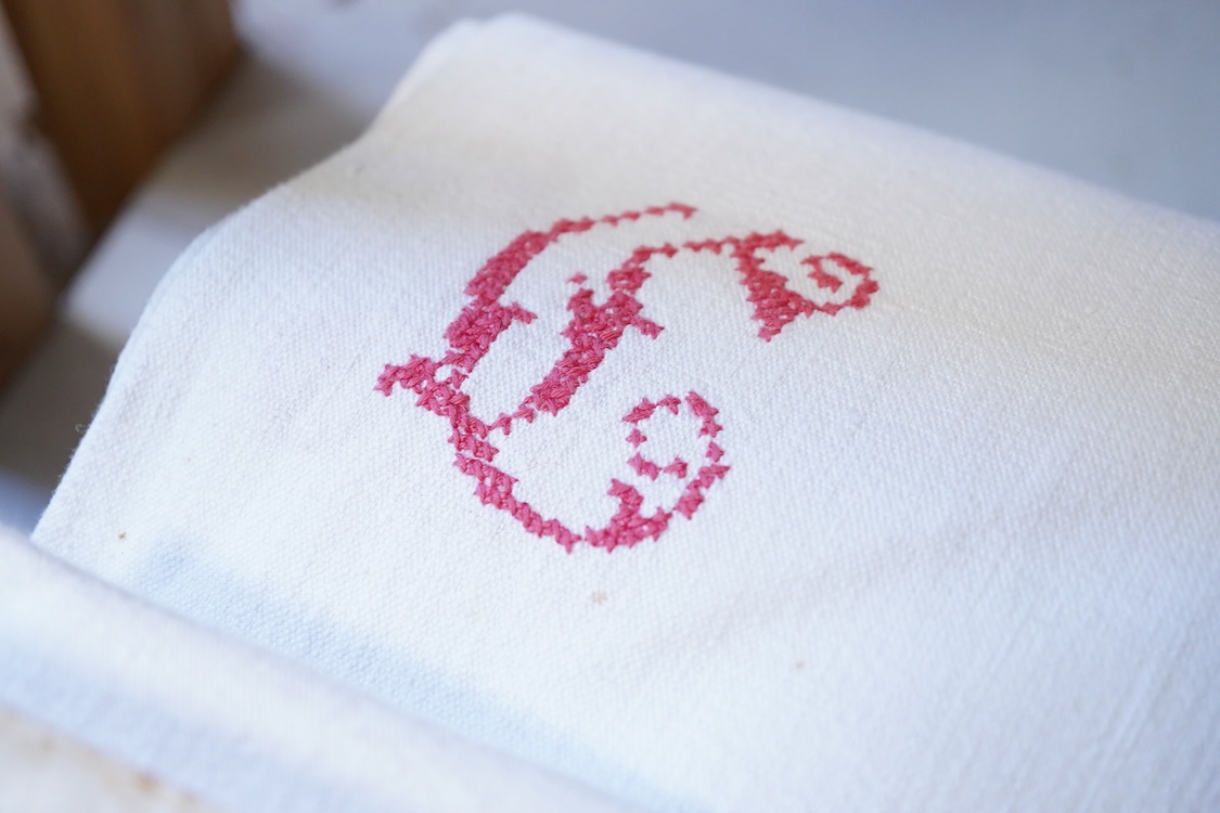 Six French provincial linen sheets each with a red cross stitched monogram to the turn back.